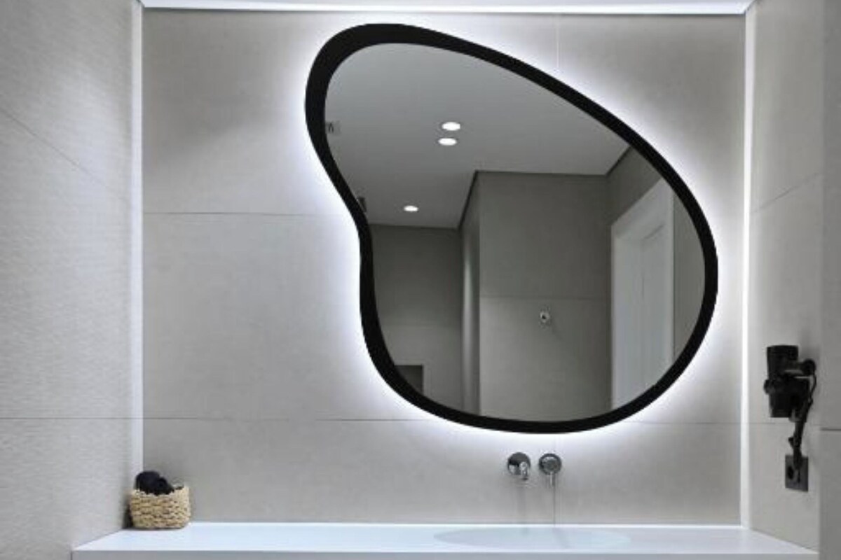 A modern bathroom with a white sink, a mirror with a black frame, and a wooden shelf below the sink.