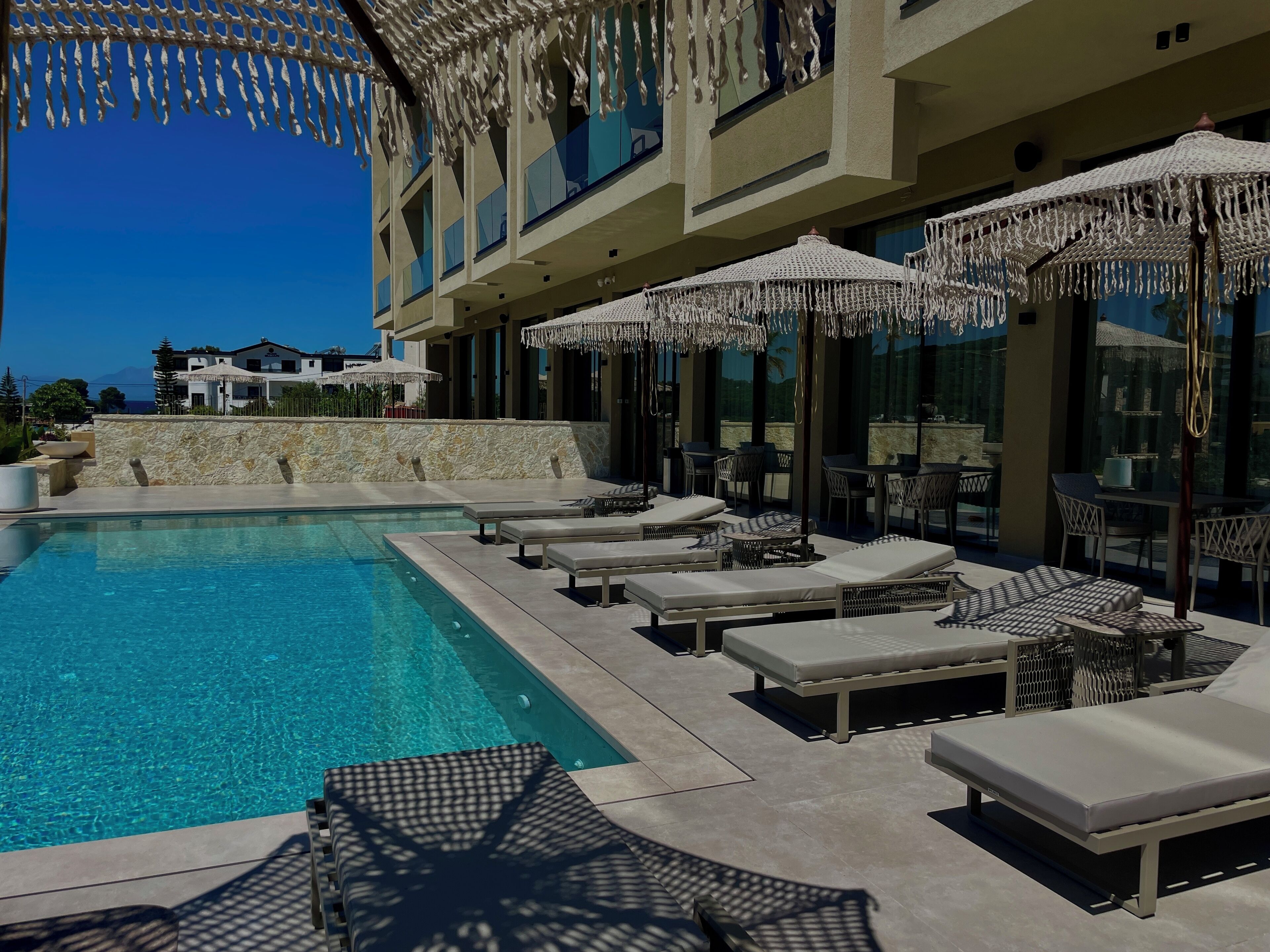 A poolside area with lounge chairs and umbrellas, a stone wall, and a building with large windows.