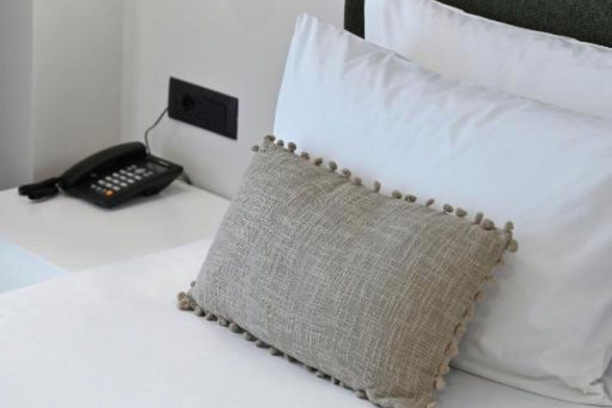 A neatly made bed with white and grey pillows, a black telephone on the side, and a wall-mounted light fixture.
