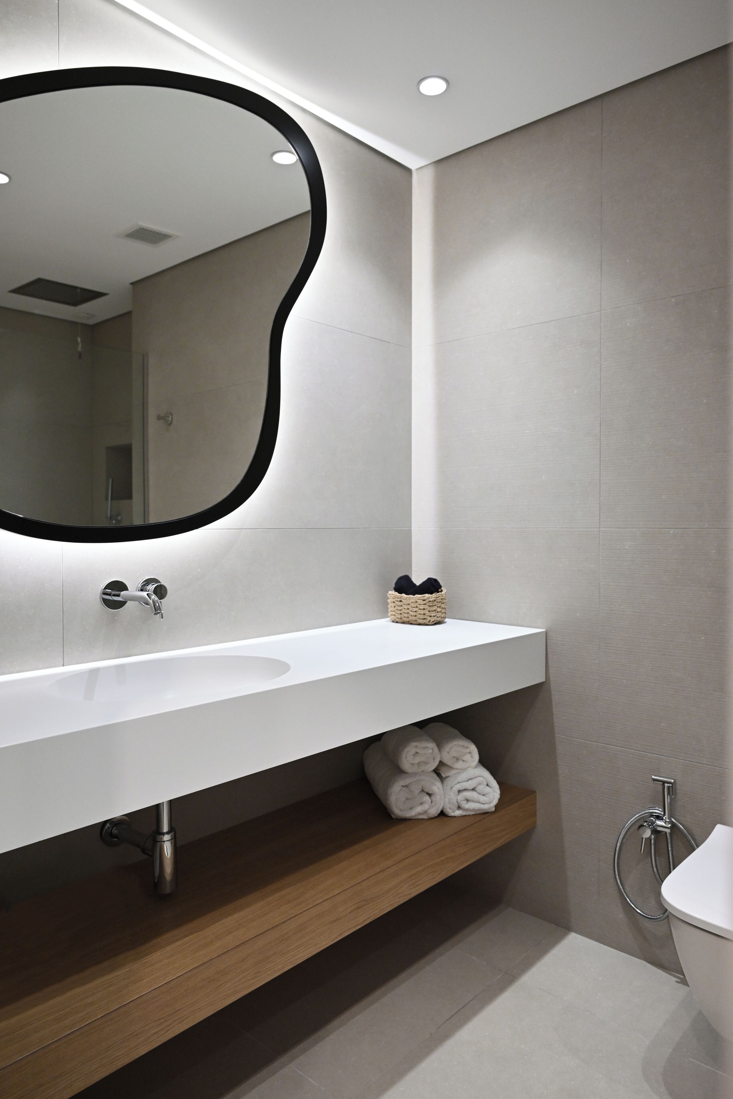 A modern bathroom with a white vanity, a large mirror with a black frame, and a wooden shelf below the sink.
