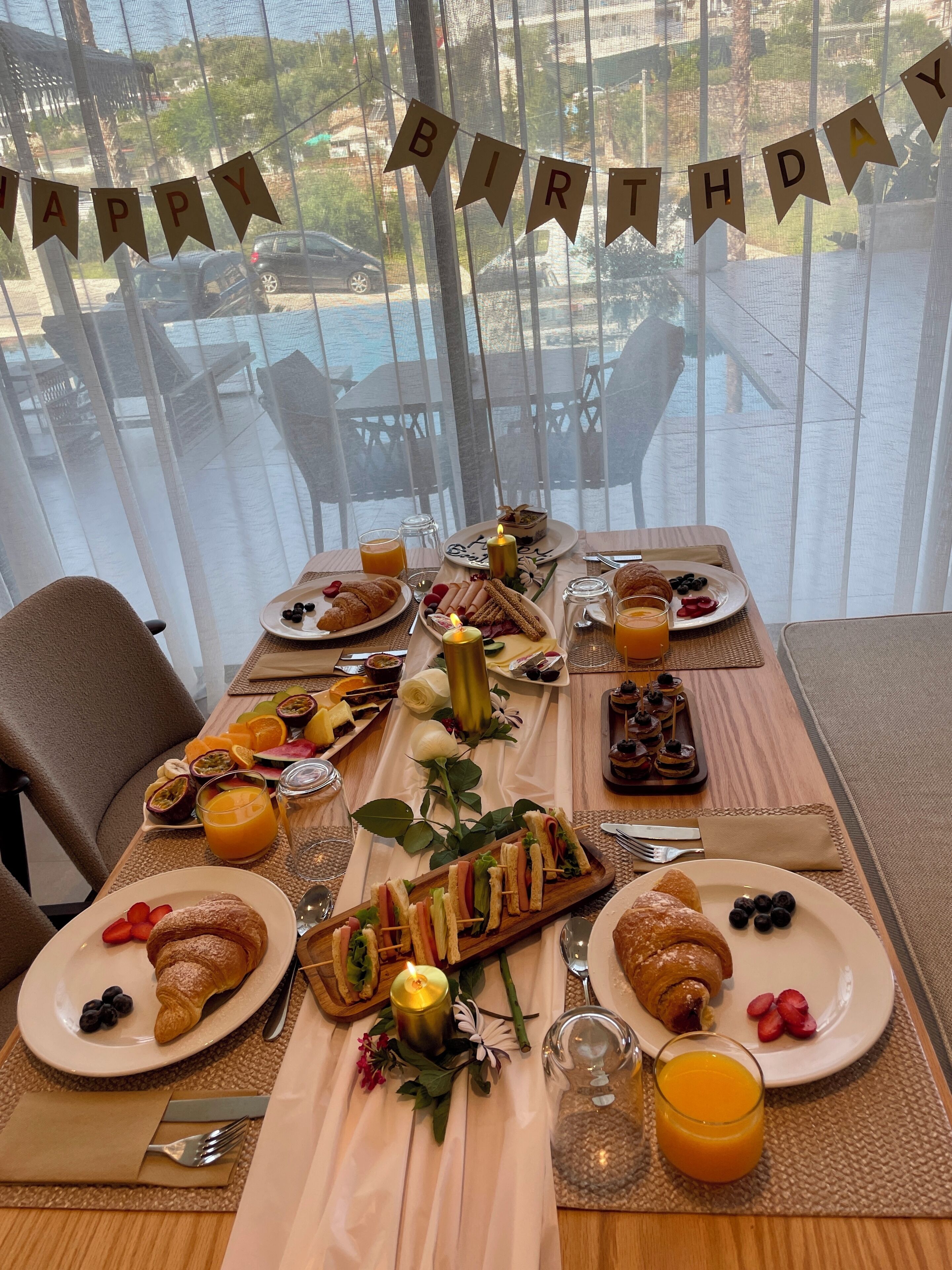 Una mesa de desayuno con un cartel que dice 'HAPPY BIRTHDAY', platos de comida y un centro de mesa con velas.