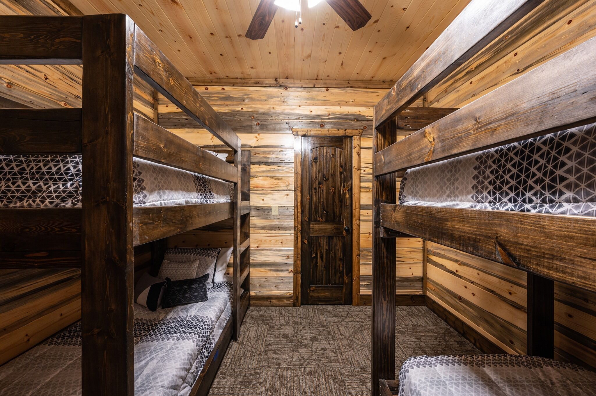 A wooden cabin interior with bunk beds, a wooden door, and a ceiling fan.