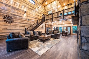 A spacious living area with a wooden interior, a staircase leading to an upper level, and a dining area with a view of the outdoors. - The Rusty Windmill In Broken Bow/ Hochatown (Broken Bow)