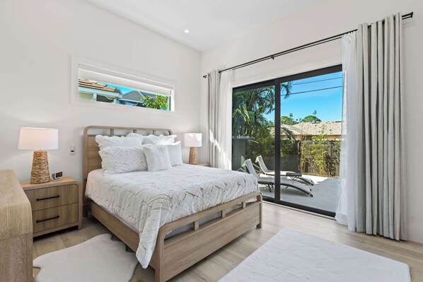 Un dormitorio moderno con una cama grande, lámparas de noche, una mesita de noche y vistas a un balcón con mobiliario exterior.