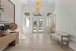 A spacious hallway with a wooden bench, a potted plant, and a large framed artwork on the left. - Brand New Gulf Coast Luxury Getaway (Naples)