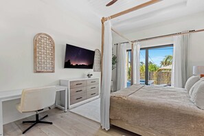 Ein Schlafzimmer mit einem Himmelbett, einem Schreibtisch mit Stuhl, einem Fernseher und Blick ins Freie.