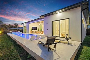 A modern house with a swimming pool, outdoor seating, and a TV in the living room. - Brand New Gulf Coast Luxury Getaway (Naples)