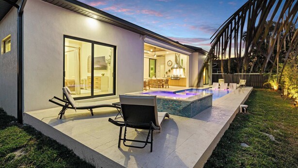 A modern house with a swimming pool, outdoor seating, and a kitchen visible through the glass doors. - Brand New Gulf Coast Luxury Getaway (Naples)