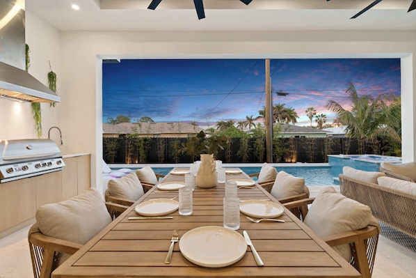 A dining area with a view of a swimming pool and sunset.