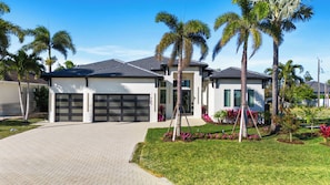 A modern two-story house with a garage, surrounded by palm trees and a well-maintained lawn.