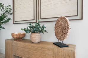 A wooden console table with a woven bowl, a potted plant, and a wooden sculpture.