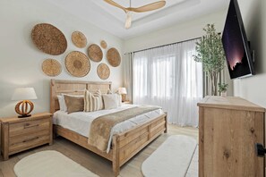 A bedroom with a wooden bed, bedside tables, a ceiling fan, a TV, and decorative woven wall hangings.