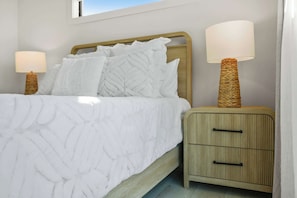 Una cama bien hecha con cabecera de madera, dos lámparas de noche y una mesita de noche de madera con cajones.