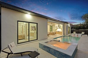 Ein modernes Haus mit Swimmingpool, Essbereich und einem Schlafzimmer, die durch große Schiebetüren sichtbar sind.