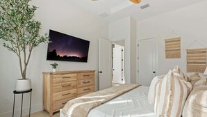 A bedroom with a bed, a night sky painting, a wooden dresser, and a potted plant. - Brand New Gulf Coast Luxury Getaway (Naples)