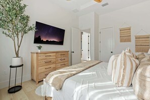 Une chambre à coucher avec un lit, un tableau représentant un ciel étoilé, une commode en bois et une plante en pot.