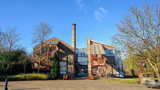 A historic building with a tall chimney, a glass entrance, and a brick facade. - Bay Tree Cottage Rhondda Valley by STAE-Homes (Rhondda Cynon Taff)