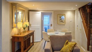A well-lit hallway with a wooden console table, a sofa with a patterned cushion, and a dining area with a white table and chairs. - Bay Tree Cottage Rhondda Valley by STAE-Homes (Rhondda Cynon Taff)