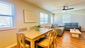 Amplia sala de estar con mesa de comedor de madera, sillas, sofá gris y ventilador de techo.