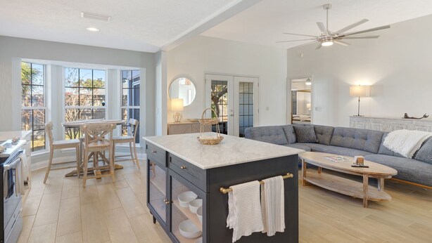 A spacious living area with a large window, a kitchen with a central island, and a grey sofa.
