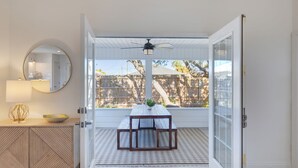 An open sliding glass door leading to a patio with a wooden table, a ceiling fan, and a view of a wooden fence.