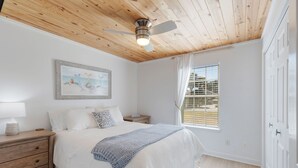 A bedroom with a wooden ceiling, a bed with white bedding, a nightstand with a lamp, a framed picture on the wall, and a window with blinds.