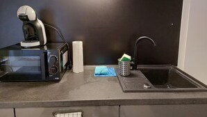 Eine kleine Küche mit Mikrowelle, Wasserkocher, Spüle und einer Arbeitsfläche.