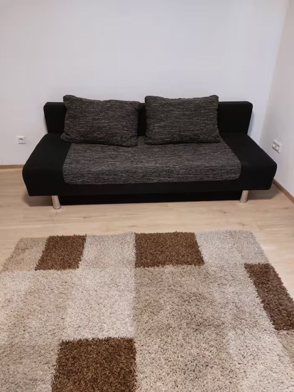 A black sofa with grey cushions and a brown and white patterned rug on a wooden floor.
