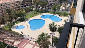 Zona residencial con complejo de piscinas, rodeada de palmeras y edificios.