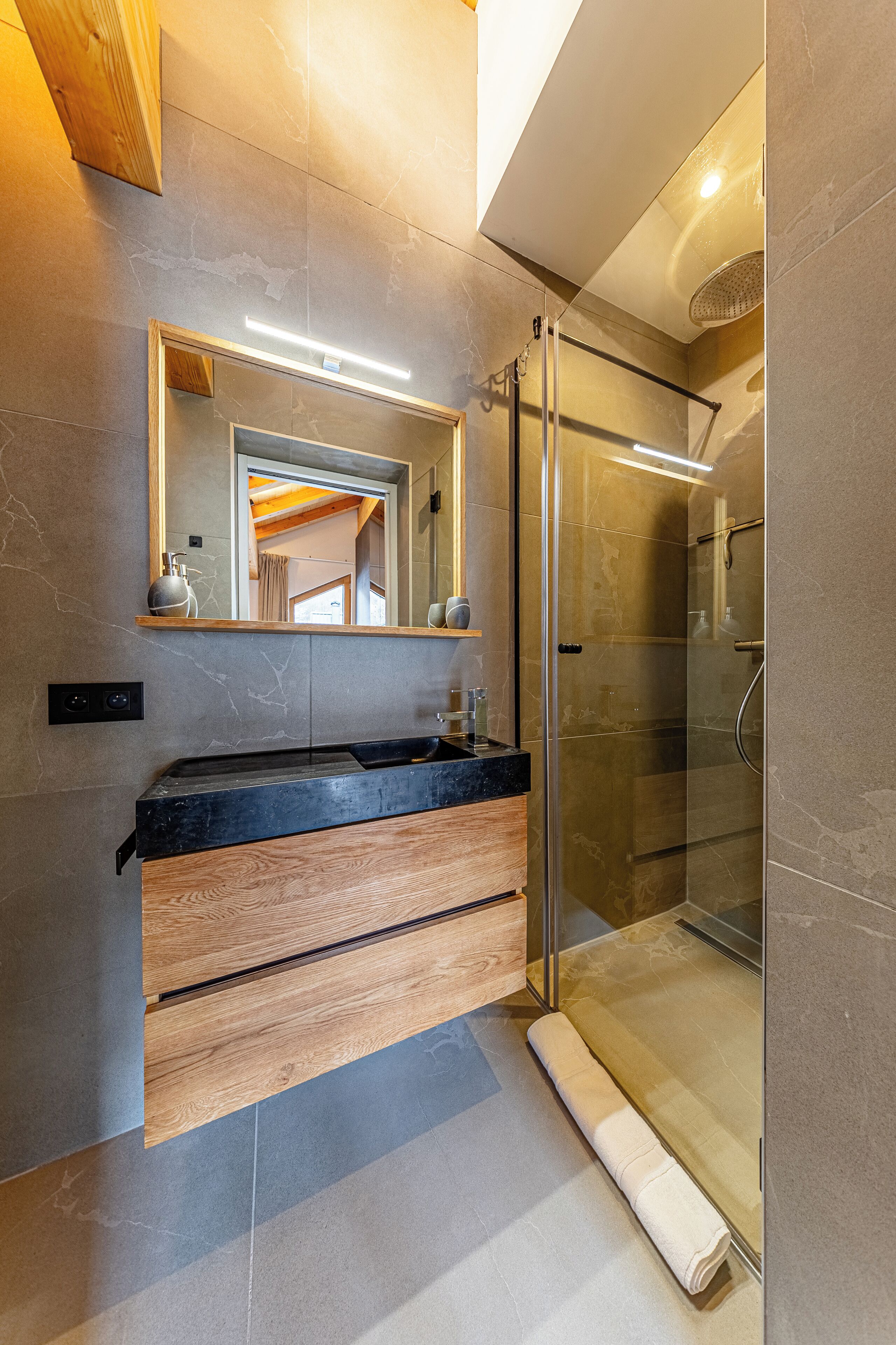 Un bagno moderno con cabina doccia in vetro, mobile lavabo in legno e uno specchio grande.