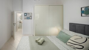 A bedroom with a bed, a grey headboard, a bedside table, and a nightstand. There is a door leading to another room. - House Runa in Porec, Croatia (Porec)