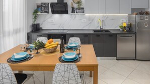 A modern kitchen with a built-in oven, a sink, and a refrigerator. There is a dining table set with blue plates and a bowl of fruit. - House Runa in Porec, Croatia (Porec)