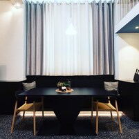 Un comedor moderno con una mesa negra, sillas de madera, un sofá negro y una planta pequeña sobre la mesa.