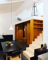 Un interior moderno con una escalera, un comedor y un pequeño rincón de estar.