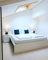 Un dormitorio moderno con una cama grande, dos mesitas de noche y un tragaluz.
