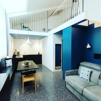 Un apartamento moderno con zona de comedor, sofá y una escalera que lleva a un nivel superior.