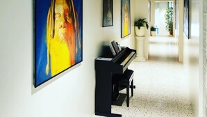 A hallway with a piano, large paintings on the walls, and a plant in the center. - Pepper Suite (Bolzano)