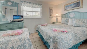 A bedroom with two beds, a TV, a desk, and a window with blinds.