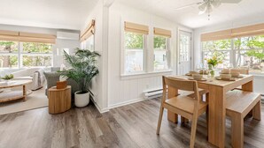 Una luminosa sala da pranzo con tavolo e sedie in legno, ampie finestre con persiane e una ventola a soffitto.