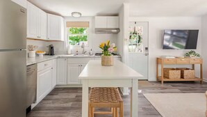 Una cucina moderna con mobili bianchi, un'isola centrale e un televisore su un supporto in legno.