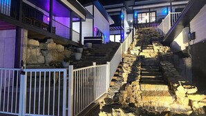 Escadaria de pedra em vários níveis que leva a um edifício com varandas, iluminada por luzes roxas e brancas.