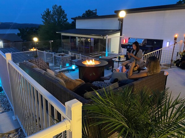 Un patio al aire libre con una chimenea, asientos y vistas al jardín trasero.