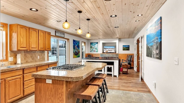 A modern kitchen with wooden cabinets, a granite countertop, and a central island with stools. - Moose Caboose Hot Tub + Schweitzer Views (Bonner County)