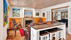 A cozy living room with a fireplace, wooden ceiling, and a dining area with a long table and benches. - Moose Caboose Hot Tub + Schweitzer Views (Bonner County)