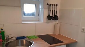 A small kitchen with a sink, a window, and a countertop. There are utensils hanging on the wall and a trash bin. - Flat Bangoua (Abstatt)