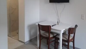 A modern room with a white table and two wooden chairs, a mounted TV, and a glass shower enclosure. - Flat Bangoua (Abstatt)