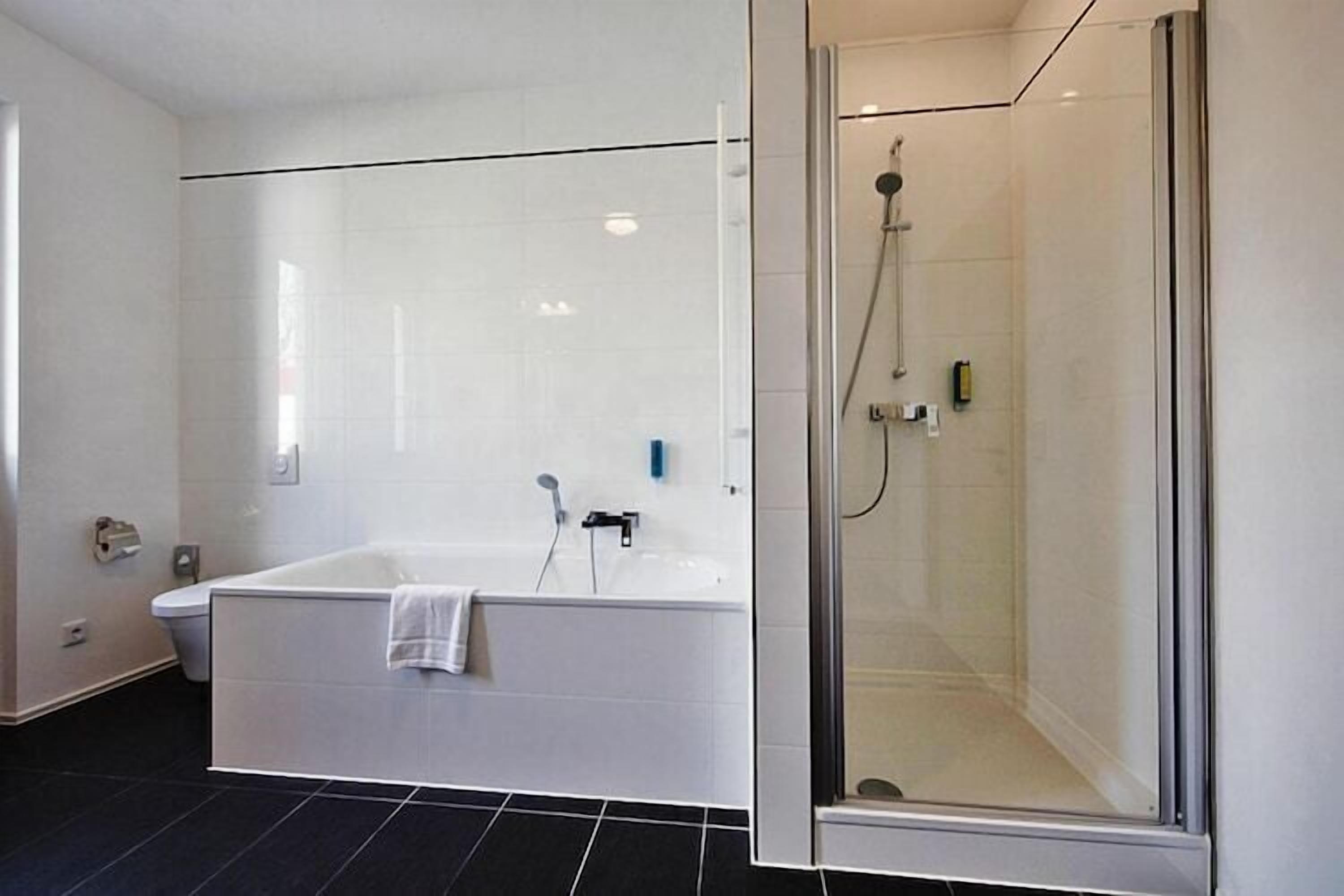 A modern bathroom with a white bathtub, a glass-enclosed shower, and black tiled flooring.