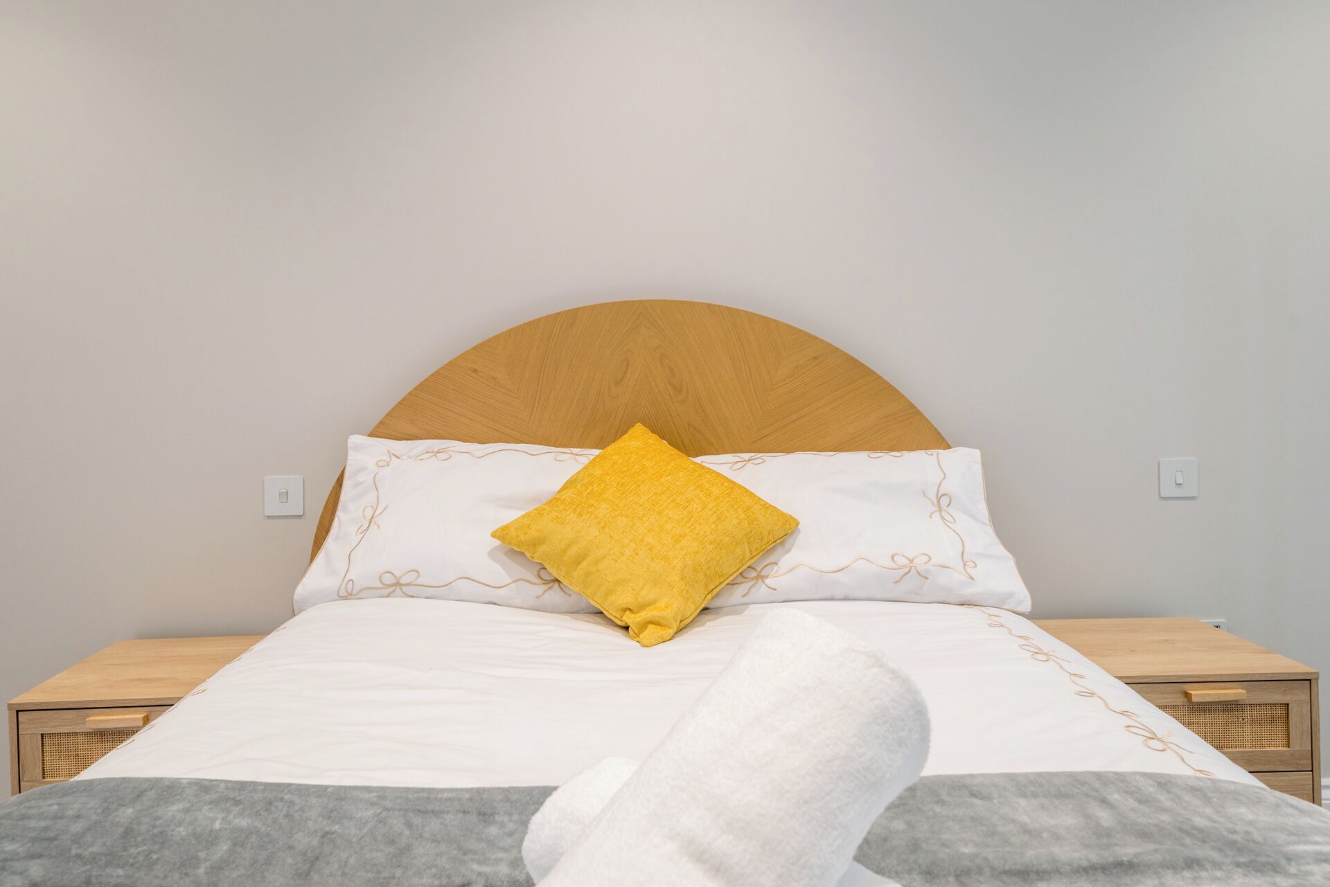Una cama bien hecha con cabecera de madera, ropa de cama blanca y una almohada amarilla.
