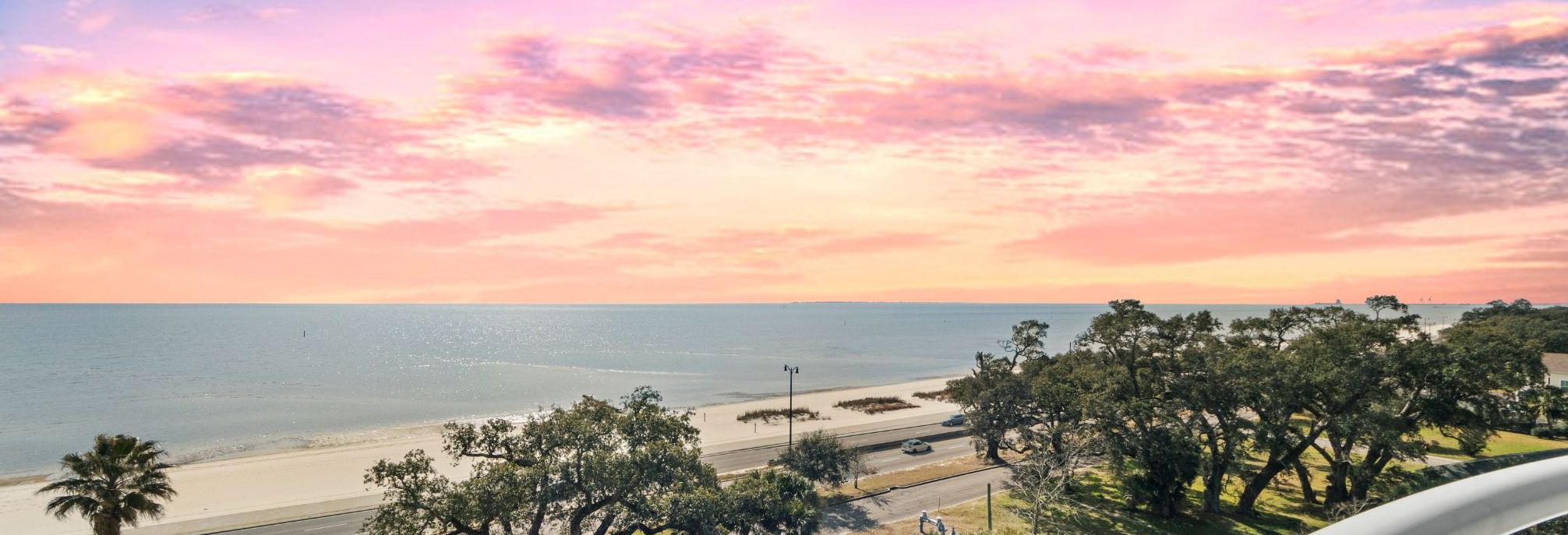 Vista da praia com uma estrada e árvores em primeiro plano.