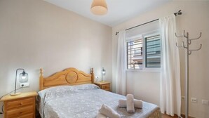 A bedroom with a wooden bed, bedside lamps, a window with curtains, and a floor lamp. - Esperanza free parking by Staycare (Rota)